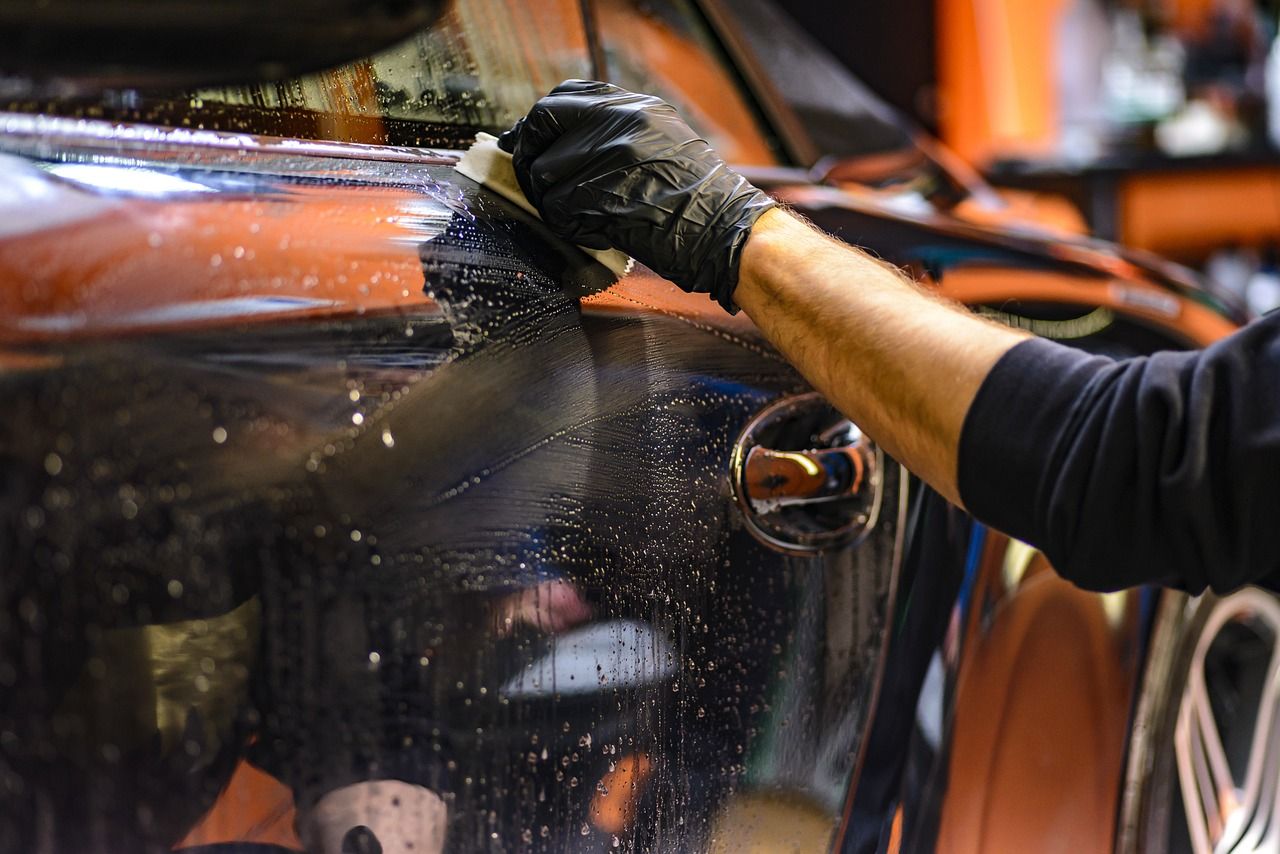 A gloved hand wiping wet, beaded paint on a dark car panel