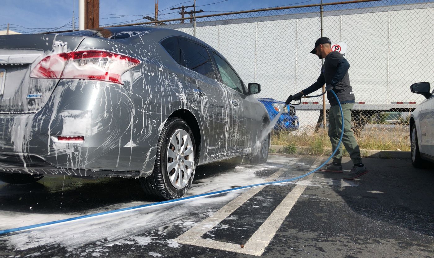 A grey saloon covered in thick white snow foam being rinsed with a pressure lance